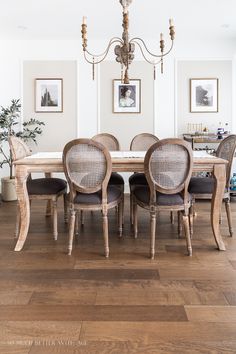 a dining room table with chairs and pictures on the wall above it, along with two chandeliers