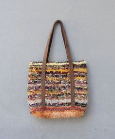 a multicolored handbag hanging on the wall with leather handles and strap around it