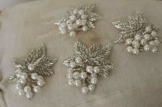 three brooches are sitting on top of a piece of cloth with pearls and leaves