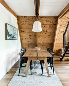 a dining room table and chairs in front of a wooden wall with stairs leading up to the second floor