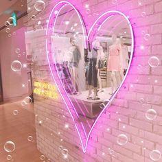 a pink heart shaped window display in front of a brick wall with bubbles floating around it