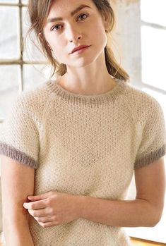 a woman standing in front of a window wearing a white sweater and beige pants with an orange belt around her waist