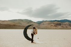 a bride and groom kissing in the desert with mountains in the background