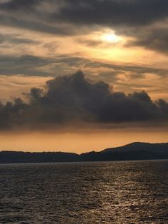 the sun is setting over the ocean with clouds in the sky and mountains behind it