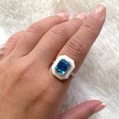 JR0271-LBT-ENWH-Y 'Queen' London Blue Topaz Emerald Cut Ring with White Enamel and Diamonds in 18K Yellow Gold Stone Size: 9 x 7 mm Approx. gemstone Wt: 2.60 Carats (London Blue Topaz) Diamonds: G-H / VS, Approx Wt: 0.23 Carats London Queen, Emerald Cut Ring, Emerald Cut Rings, Gold Stone, London Blue Topaz, London Blue, White Enamel, Emerald Cut, Blue Topaz