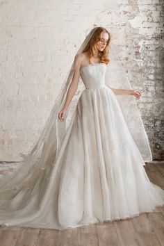 a woman wearing a wedding dress and veil in front of a brick wall with white paint