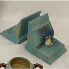 two pieces of blue pottery sitting on top of a white table next to a cup and saucer