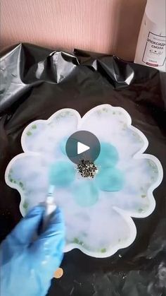 a person in blue gloves is painting a flower on a black bag with white flowers