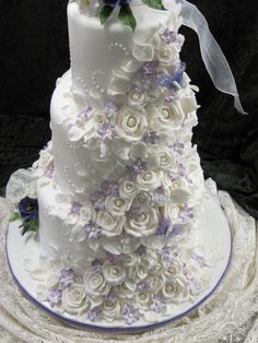 a three tiered wedding cake with white and purple flowers on the bottom, along with ribbon