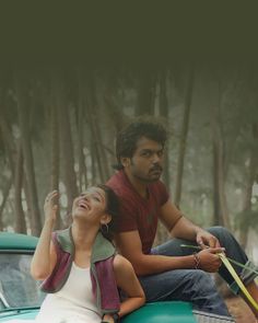 a man and woman sitting on the back of a green car in front of trees