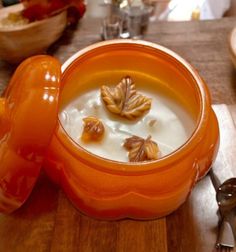 an orange bowl filled with milk and nuts on top of a wooden table next to spoons