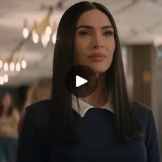 a woman with long brown hair standing in front of a chandelier and looking at the camera