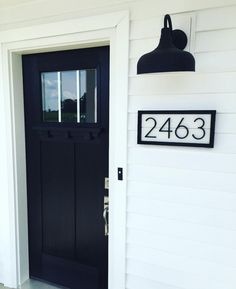 a black front door with a house number sign on the side and a light hanging above it