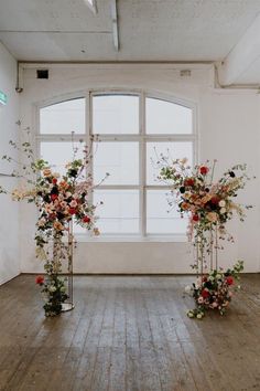 two tall vases filled with flowers sitting on top of a wooden floor next to a window