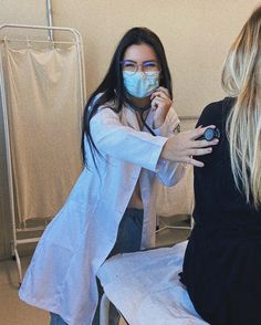 two women in white coats and masks are sitting on a bed with their hands together