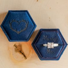 two blue velvet boxes sitting on top of a wooden table with a diamond ring in the middle