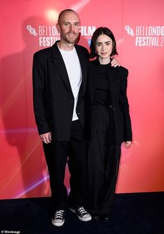 a man and woman standing next to each other in front of a red wall at the london film festival