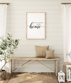 a wooden bench with two pillows on it in front of a white wall and some plants