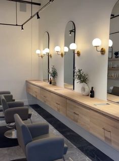 a row of chairs sitting in front of a counter with mirrors and lights on it