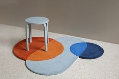 three different colored rugs on the floor with one sitting on a stool and another standing up