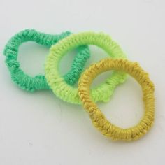 three small crocheted hair ties on a white surface, one is green and the other is yellow