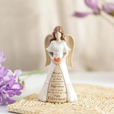 an angel figurine sitting on top of a table next to purple flowers