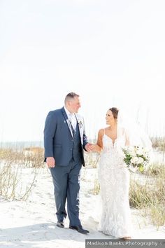 the bride and groom are walking on the beach in front of the sand dunes at their wedding