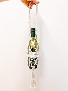 a hand holding a wine bottle in a macrame hanging from a wall hook