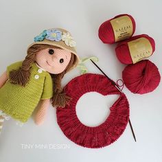 a knitted doll sitting next to a yarn wreath and knitting needles