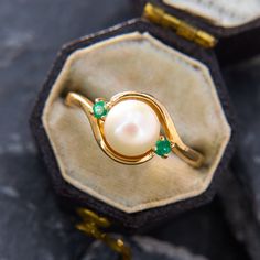 a ring with pearls and emeralds sits in an open box on top of some rocks