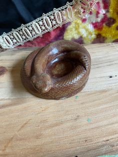 a brown snake on a wooden table next to a piece of wood and a decorative object