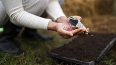 a person holding something in their hand while sitting on the ground next to some grass