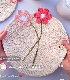 a person holding a crocheted flower on top of a white plate with pink and red flowers