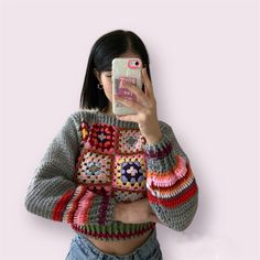 a woman taking a selfie with her cell phone wearing a crocheted sweater