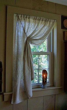 a window with a curtain hanging from it's side and a lit candle in front of it