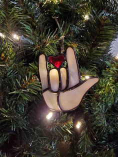 a stained glass hand ornament hanging from a christmas tree with lights on it