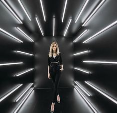 a woman standing in front of a black wall with neon lights on the sides and her legs crossed