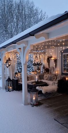 a covered patio with christmas lights on the ceiling and furniture in the snow outside at night