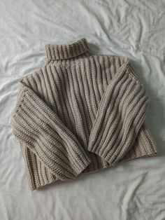 a knitted sweater laying on top of a white bed sheet with the hood pulled up