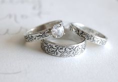 two wedding rings with one diamond on top and the other set in white gold, sitting on a piece of paper