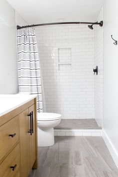 a white toilet sitting next to a wooden cabinet in a bathroom under a shower curtain