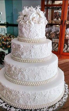 a large white wedding cake with flowers and pearls on the bottom tier is sitting on a table