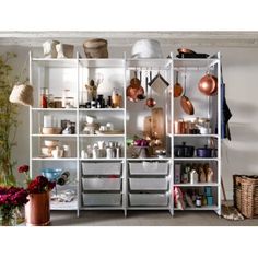 a white shelf filled with pots and pans on top of wooden floor next to plants