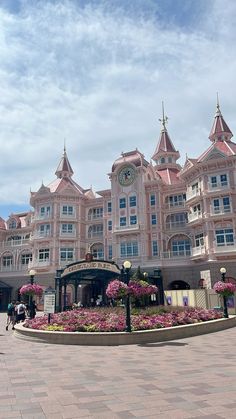 a large pink building with lots of windows and flowers in the foreground on a sunny day