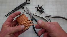 two hands are holding scissors and an orange piece of leather next to some other tools