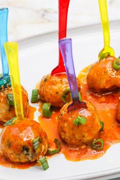 some meatballs with sauce and toothpicks on a white plate in front of other food items