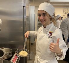 a woman in a chef's uniform is holding a spoon and giving the thumbs up