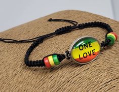 "Rasta Bracelet. One Love Bracelet. Black Braided Bracelet with Rasta wooden beads, Glass Charm with ONE LOVE Design and Rasta Flag Color. Rasta Glass Charm: 1\" Inch x 3/4\" Inch Adjustable Bracelet with sliding knot and cords. Adjust from 6\" Inches up to 10\" Inches Around the Wrist. Fist Most Sizes. Unisex Design The black cord is soft and comfort fit. FAST SHIPPING! Visit my Etsy Shop to see more Handmade Jewelry! At Freedom Lifestyle Jewelry you will find a variety of Necklaces, Bracelets Nickel-free Black Charm Bracelet As Gift, Adjustable Nickel-free Black Charm Bracelet, Nickel-free Black Charm Bracelet For Gift, Adjustable Black Bangle Charm Bracelet, Nickel-free Black Bracelet Gift, Black Bangle Friendship Bracelets As Gift, Black Friendship Bracelets As Gifts, Black Bangle Friendship Bracelets, Black Bangle Friendship Bracelet Gift