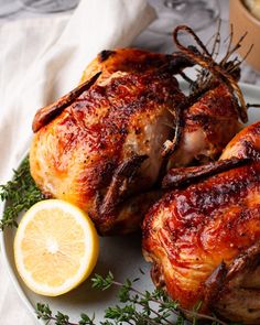 two whole chickens on a plate with lemons and herbs