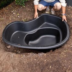 a man kneeling down next to a large black bathtub in the middle of dirt